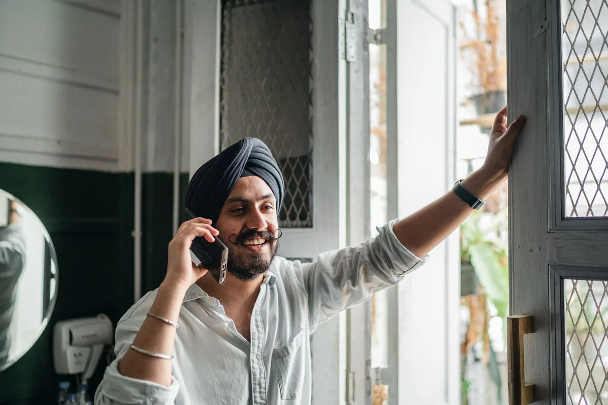 A man standing in an open doorway of a home, smiling while taking a call on his mobile phone.