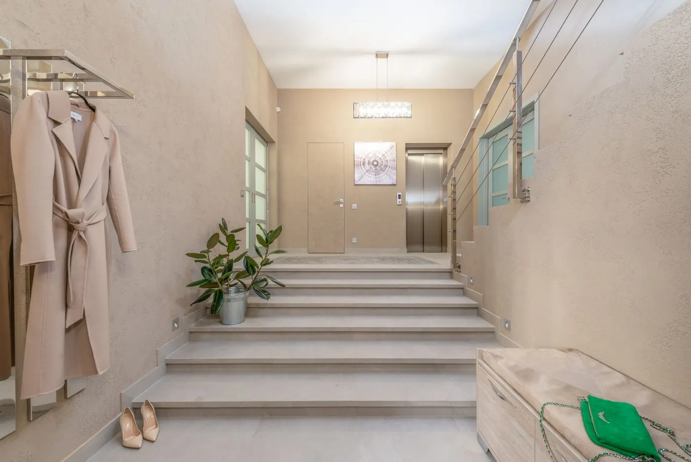 A modern apartment building entrance hall with a staircase and a metal elevator door at the far end.