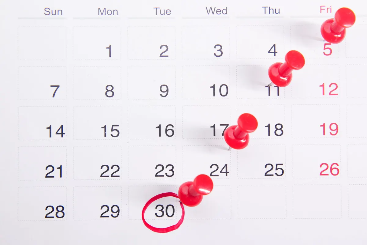 A wall calendar with red push pins marking several dates and one date circled in red pen.