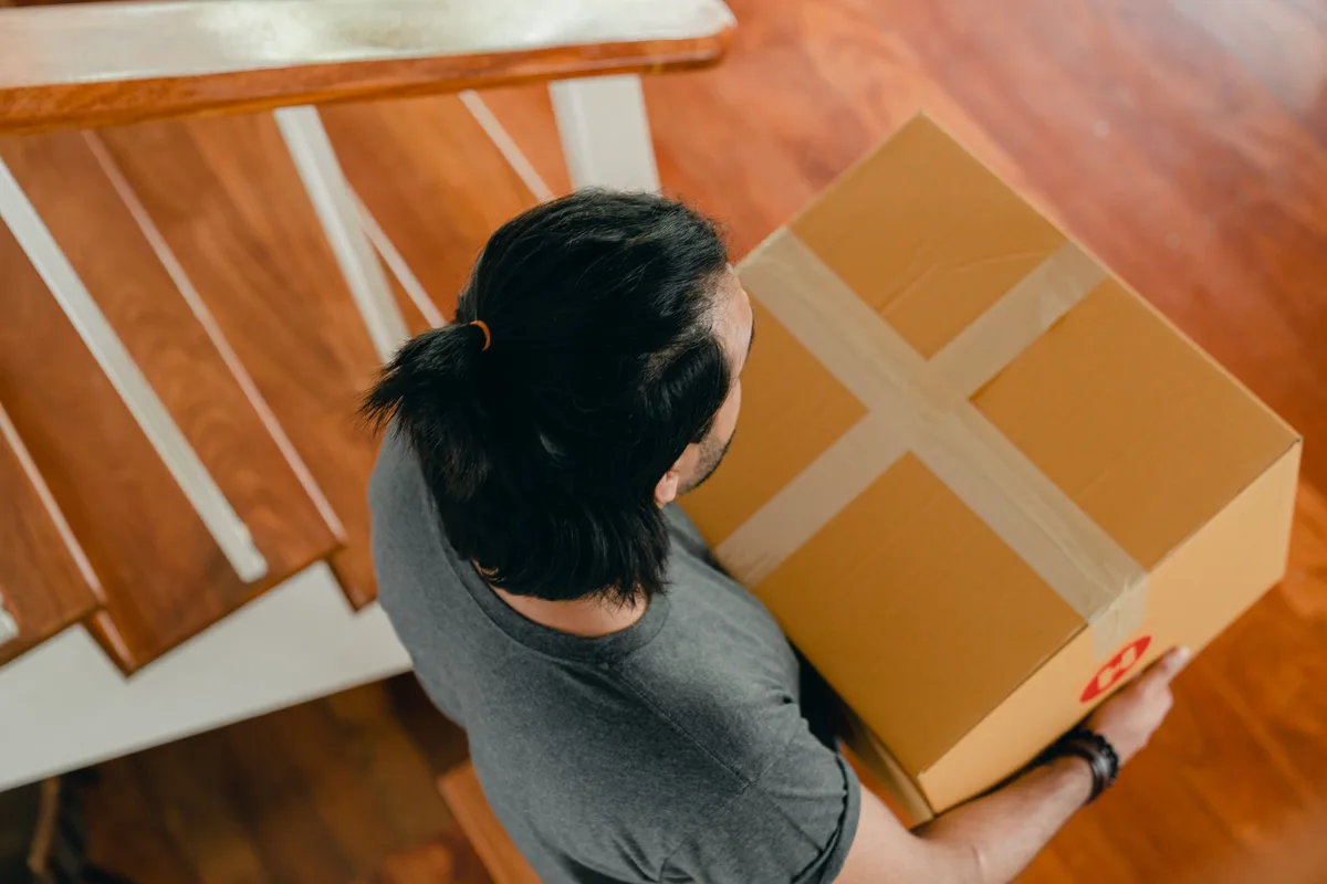 An overhead view of a person carrying a single taped cardboard box down a staircase.