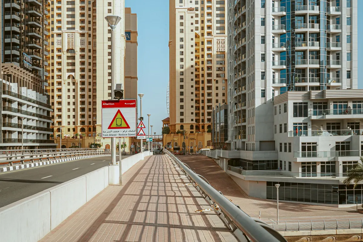 An empty pedestrian walkway running between residential high-rise towers in Dubai under a clear sky.
