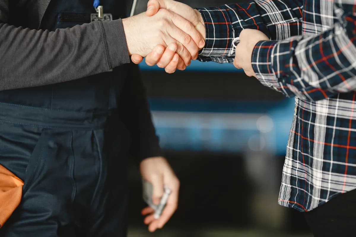Close-up of a worker in overalls shaking hands with a customer.