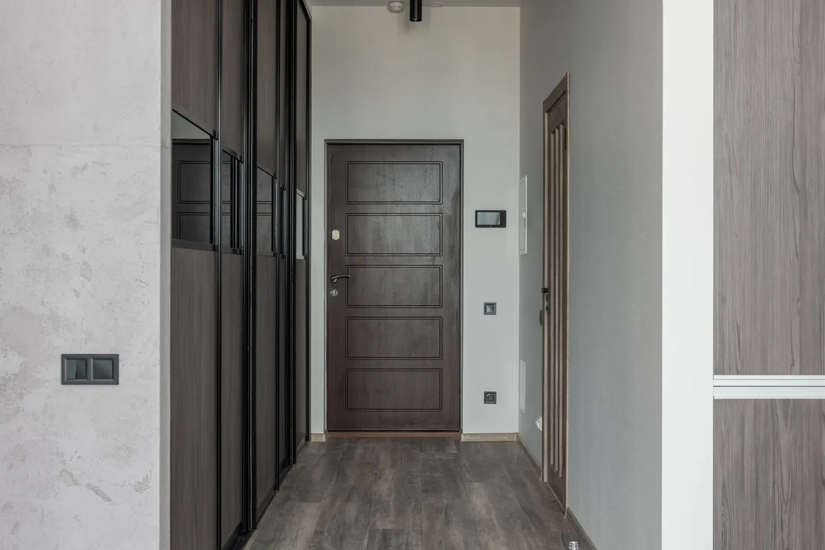A narrow apartment hallway lined with a full-height fitted wardrobe, leading to a closed front door.