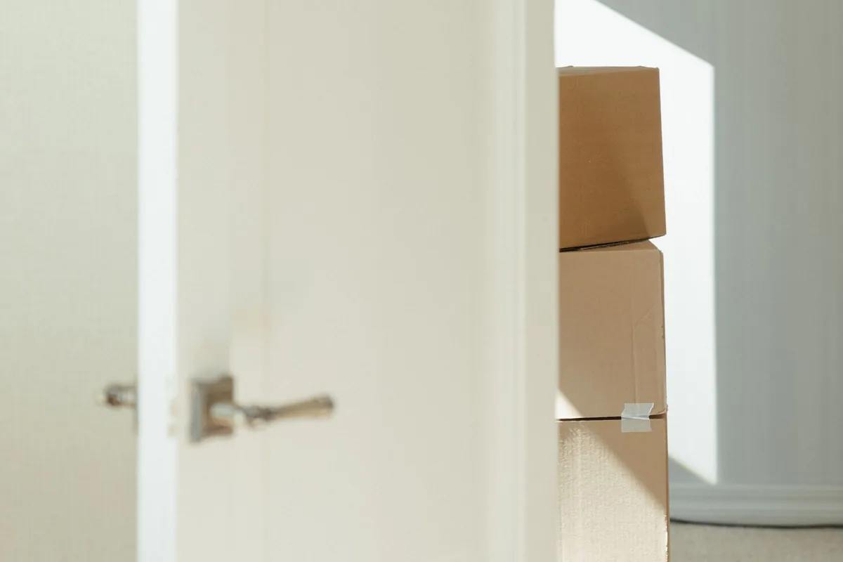 A partly open white door with a stack of sealed cardboard boxes visible in the room behind it.
