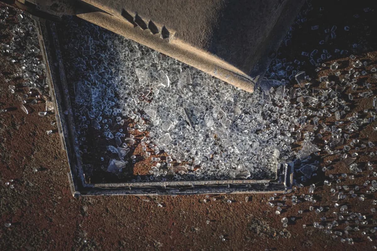 A shattered glass panel still sitting in its metal frame on the ground, with fragments scattered across the surrounding surface.