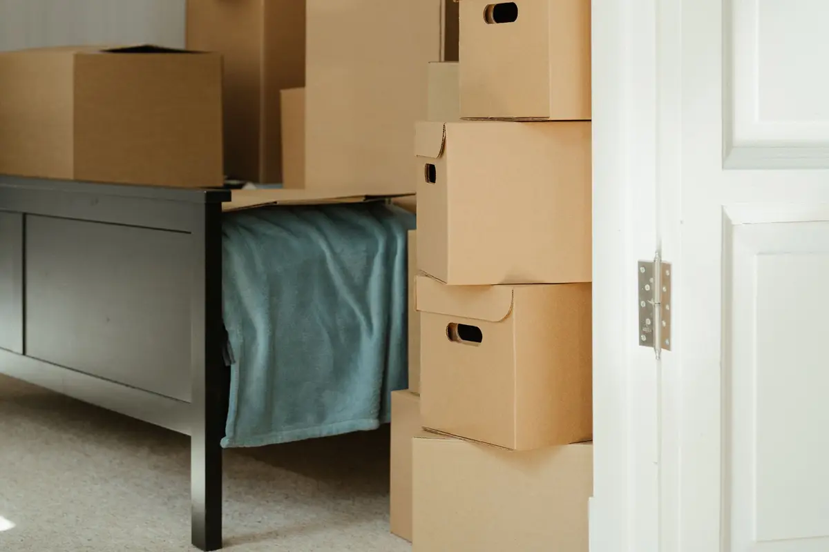 A tall stack of lidded cardboard storage boxes beside a cloth-covered bench, seen through a part-open white door.