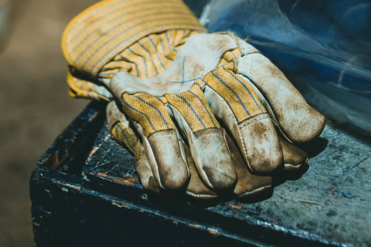 A pair of worn yellow and tan leather work gloves resting on the lid of a scuffed metal toolbox.