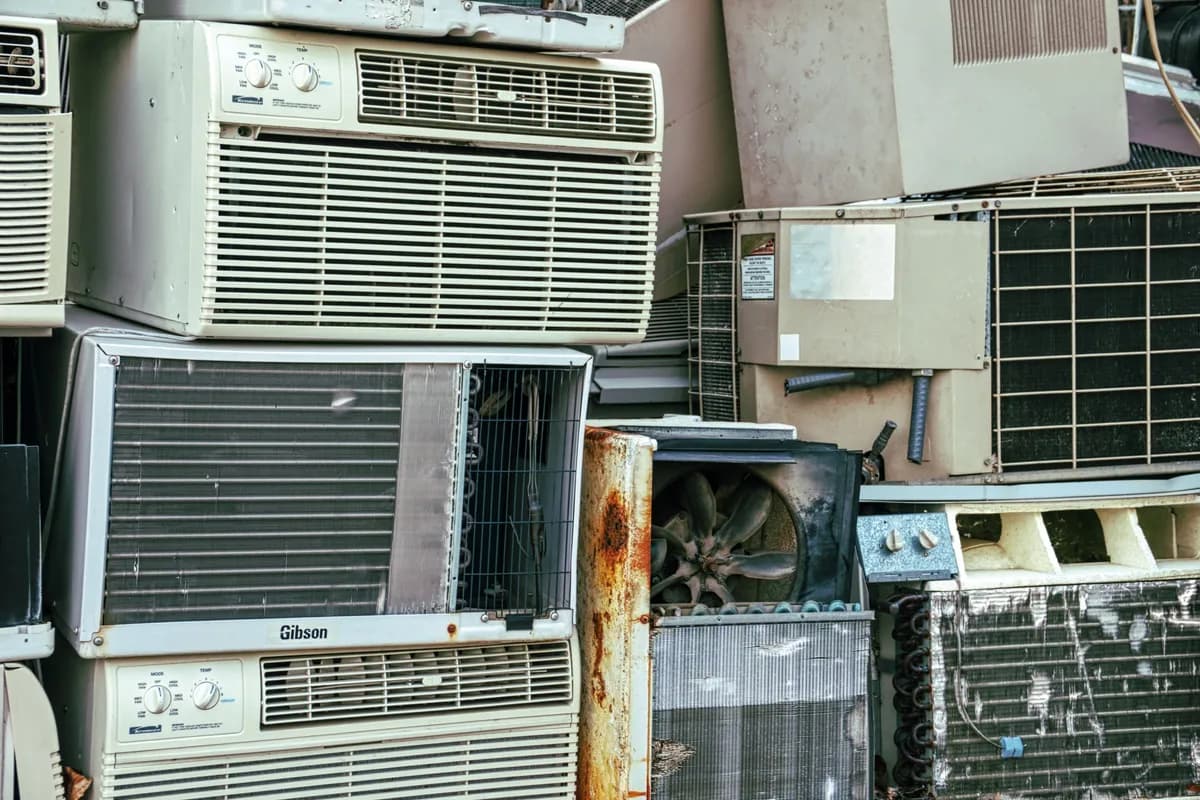 A stack of old window and wall air-conditioning units with rusted casings and exposed cooling fins, piled up outdoors.