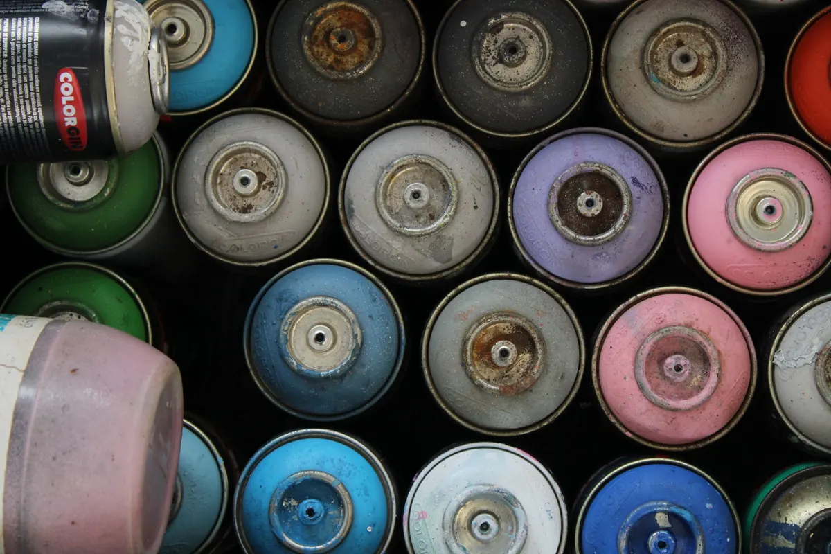 Dozens of used aerosol spray cans photographed from above, stacked upside down with paint-crusted nozzles.