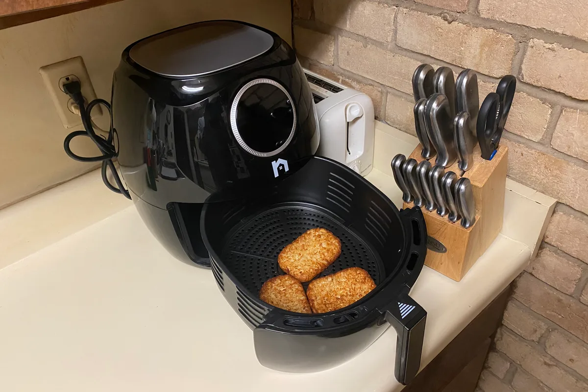 A black air fryer with its basket pulled out on a kitchen counter beside a toaster and a knife block.