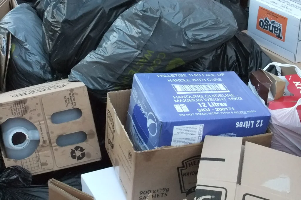Filled black rubbish bags and cardboard boxes stacked together in a cleared space, ready to be carried out.