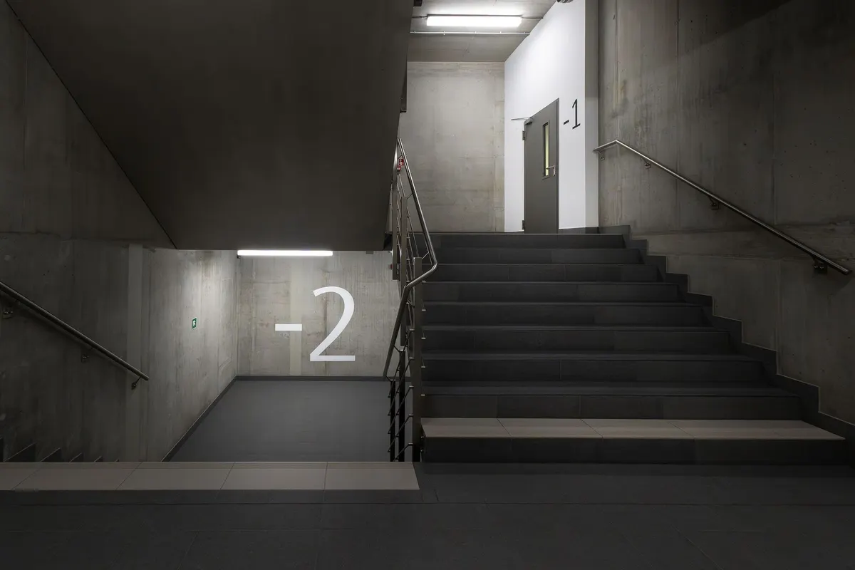 A concrete stairwell in an underground level of a building, with large painted level markings reading minus one and minus two beside the steps.