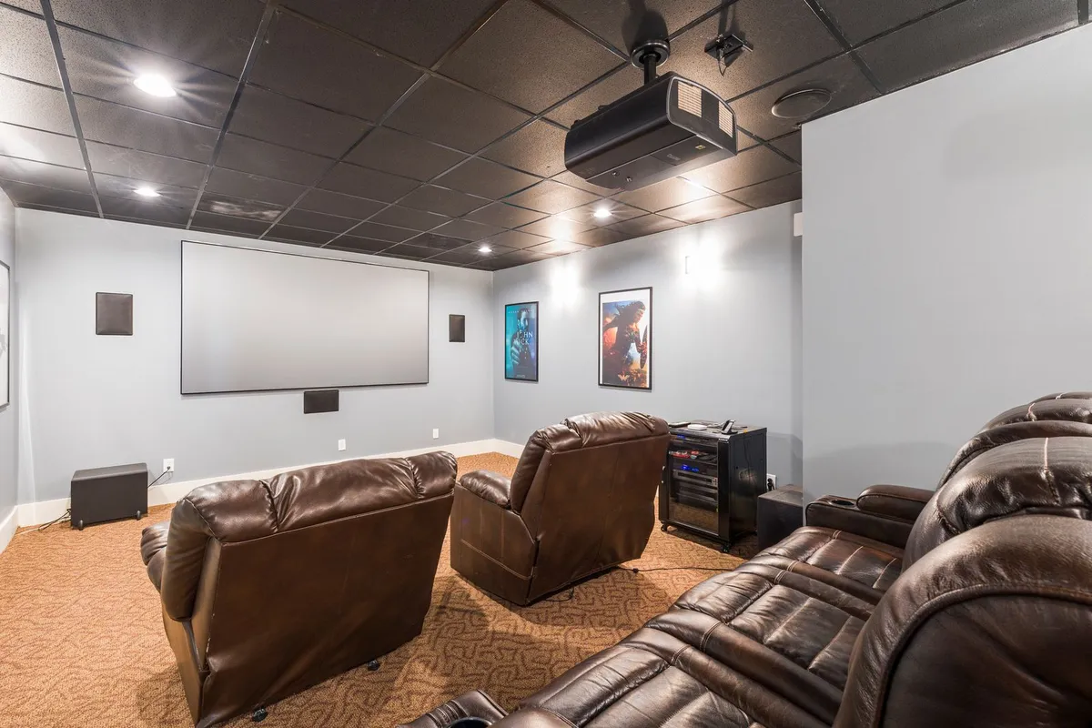 Two brown leather reclining chairs facing a projector screen in a home cinema room, with the padded backrest of a third recliner visible in the foreground.