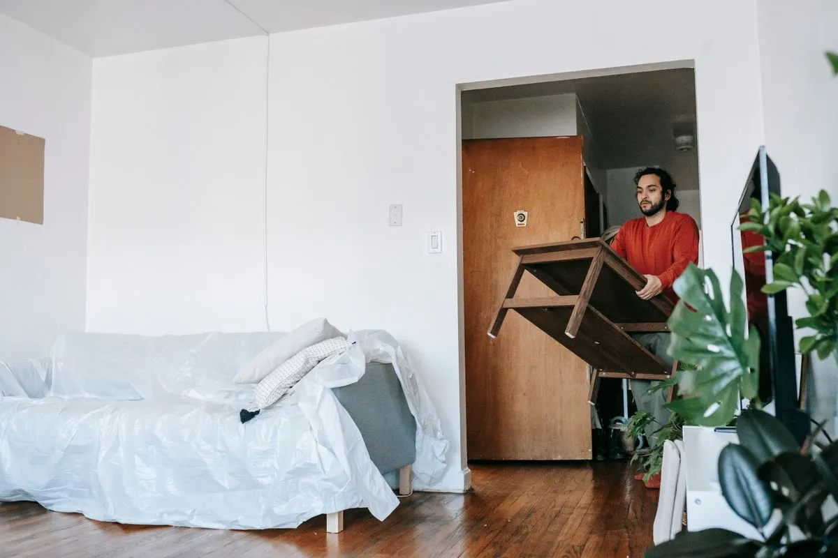 A person lifting a heavy wooden table during a home clearance.