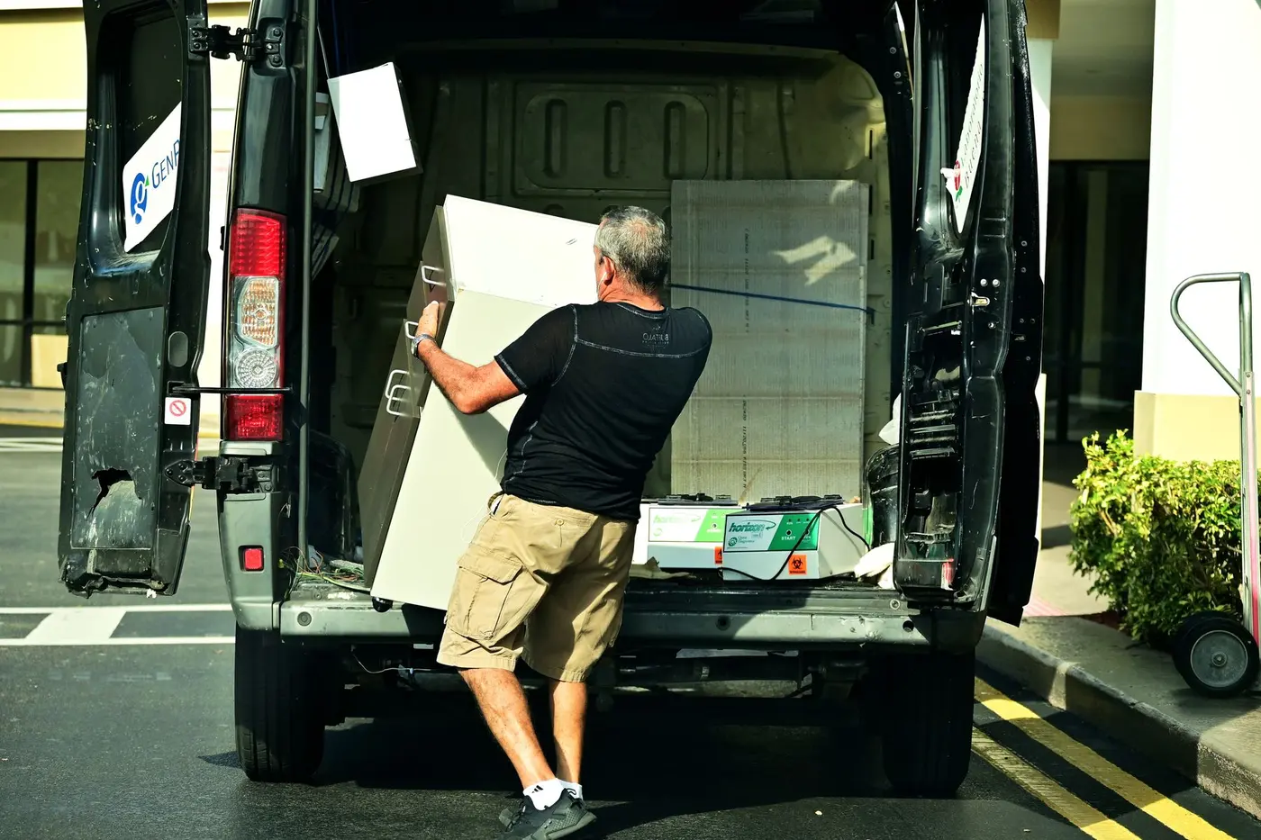 A man sliding a large white cabinet into the back of an open van parked outside a building.