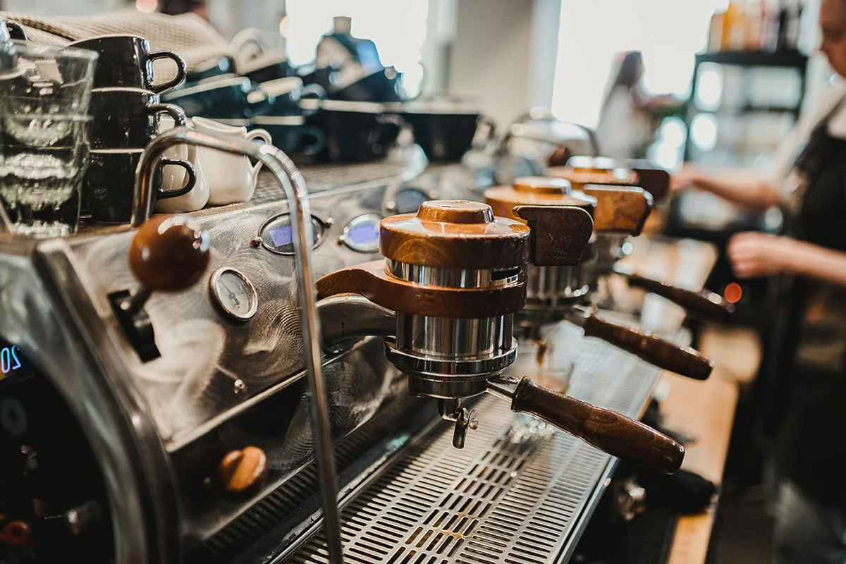 A commercial dual-group espresso machine with steam wands and portafilters resting on a cafe service counter