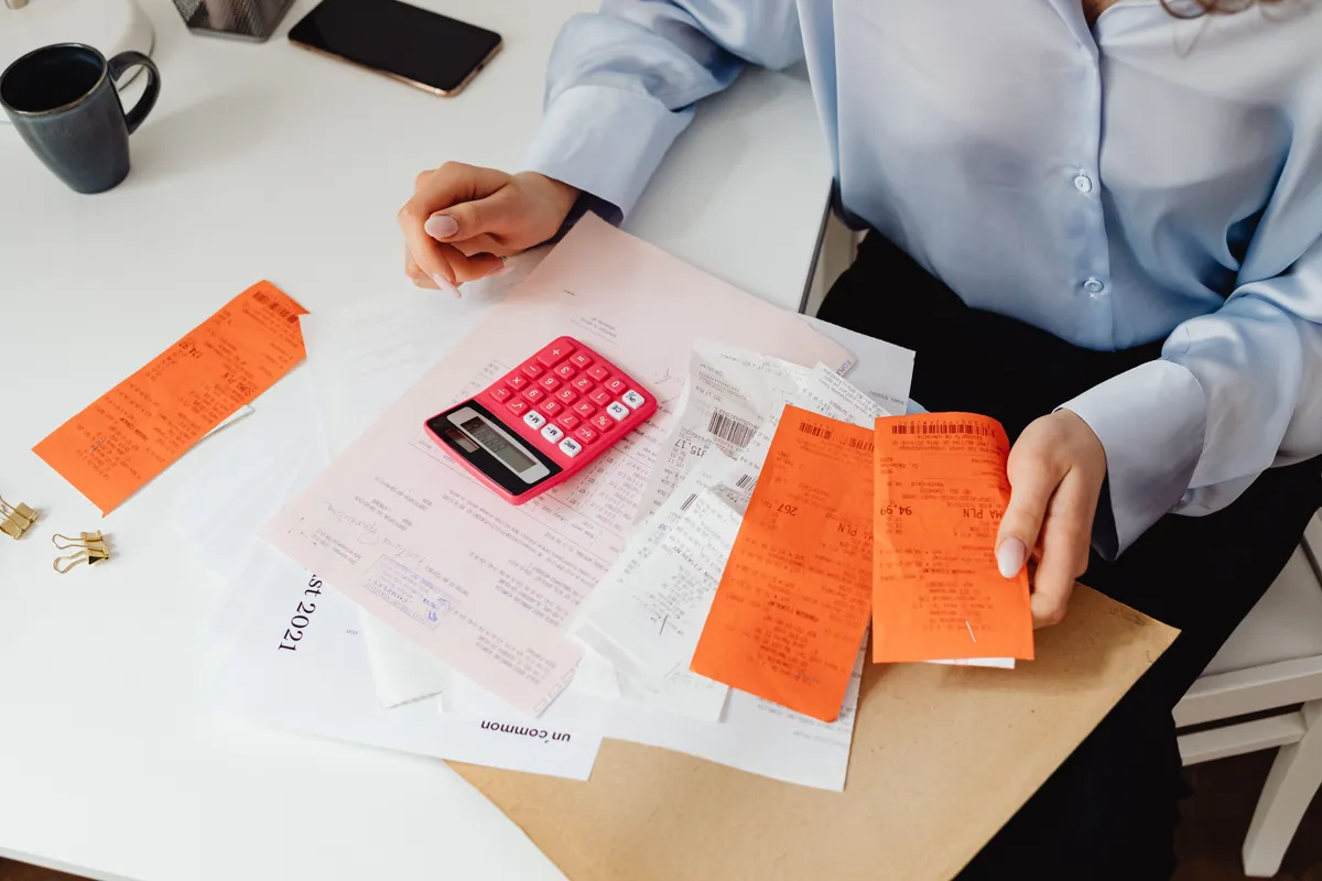 A pink calculator resting on a pile of receipts and paperwork while someone works out a budget.
