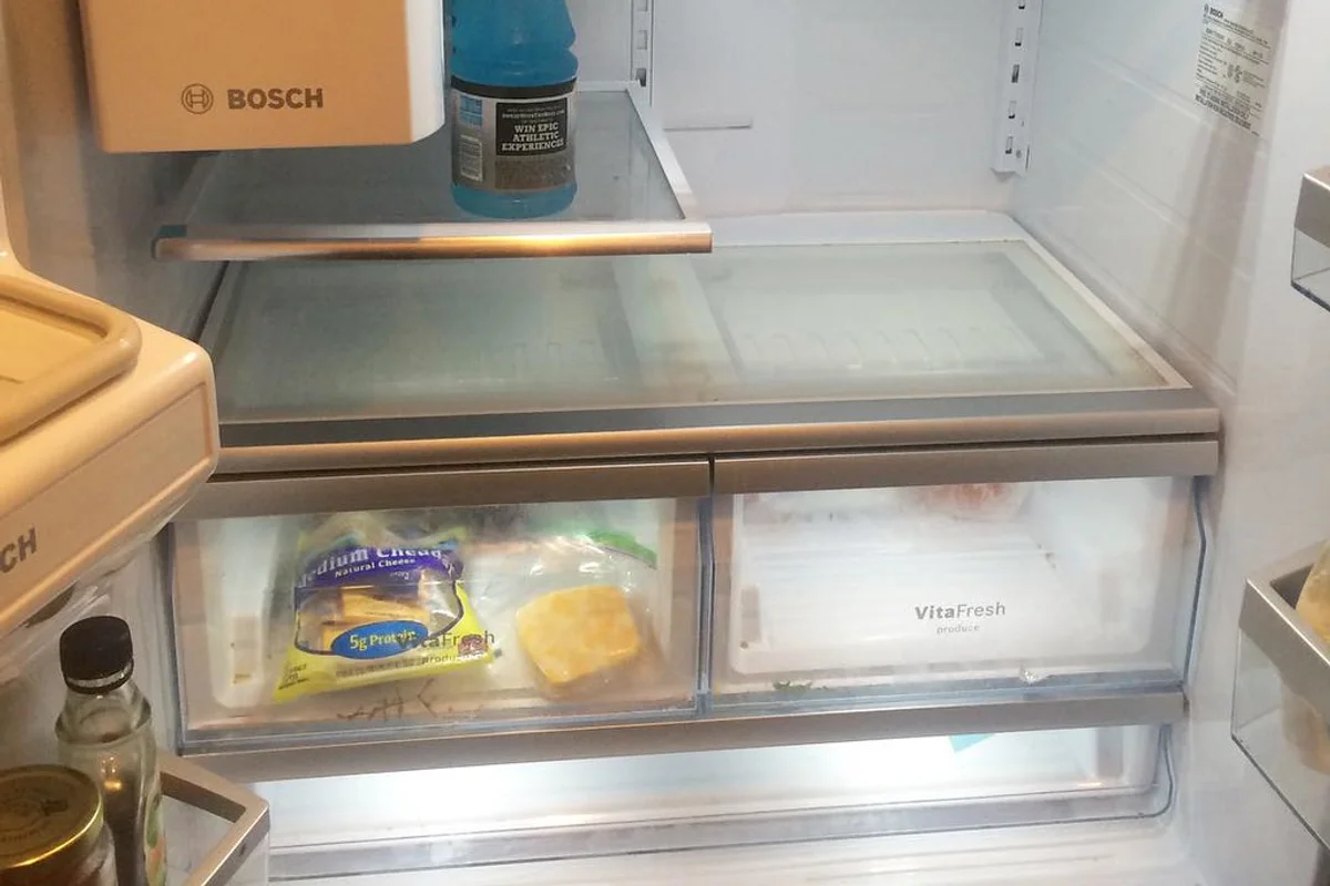 Emptied domestic refrigerator with open door showing clean glass shelves and plastic door compartments.