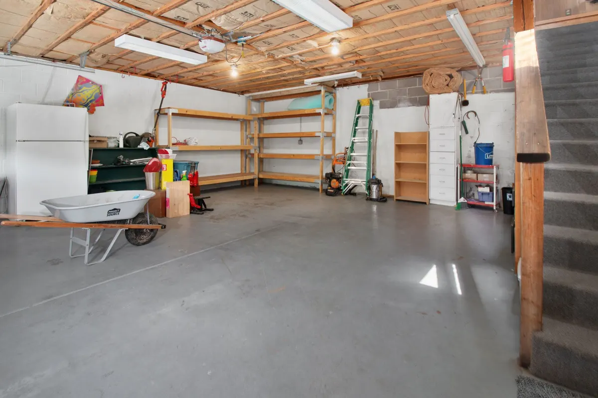 A large domestic garage cleared down to a bare concrete floor, with empty wall shelving, a step ladder and a wheelbarrow at one side.