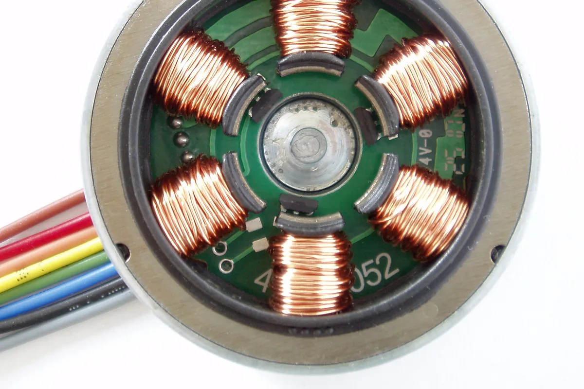 The copper windings inside a small electric motor, exposed with the cover removed and a ribbon of coloured wires leading out of it.