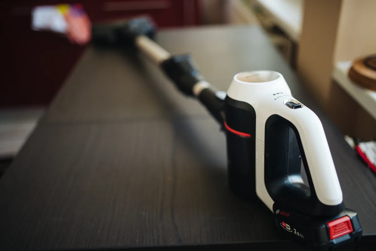 A cordless stick vacuum cleaner lying on a dark table with its removable battery pack still attached.
