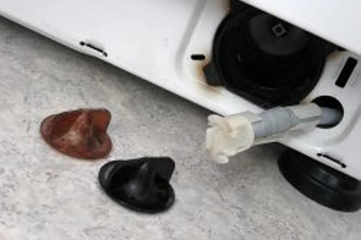 A washing machine base filter and drain hose opened to empty residual water before disconnection.