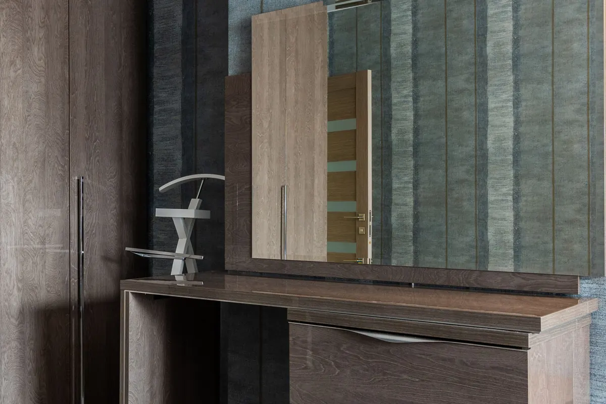 A dark wood dressing table with a stone top and a large rectangular mirror on the wall directly above it, next to a tall fitted wardrobe.