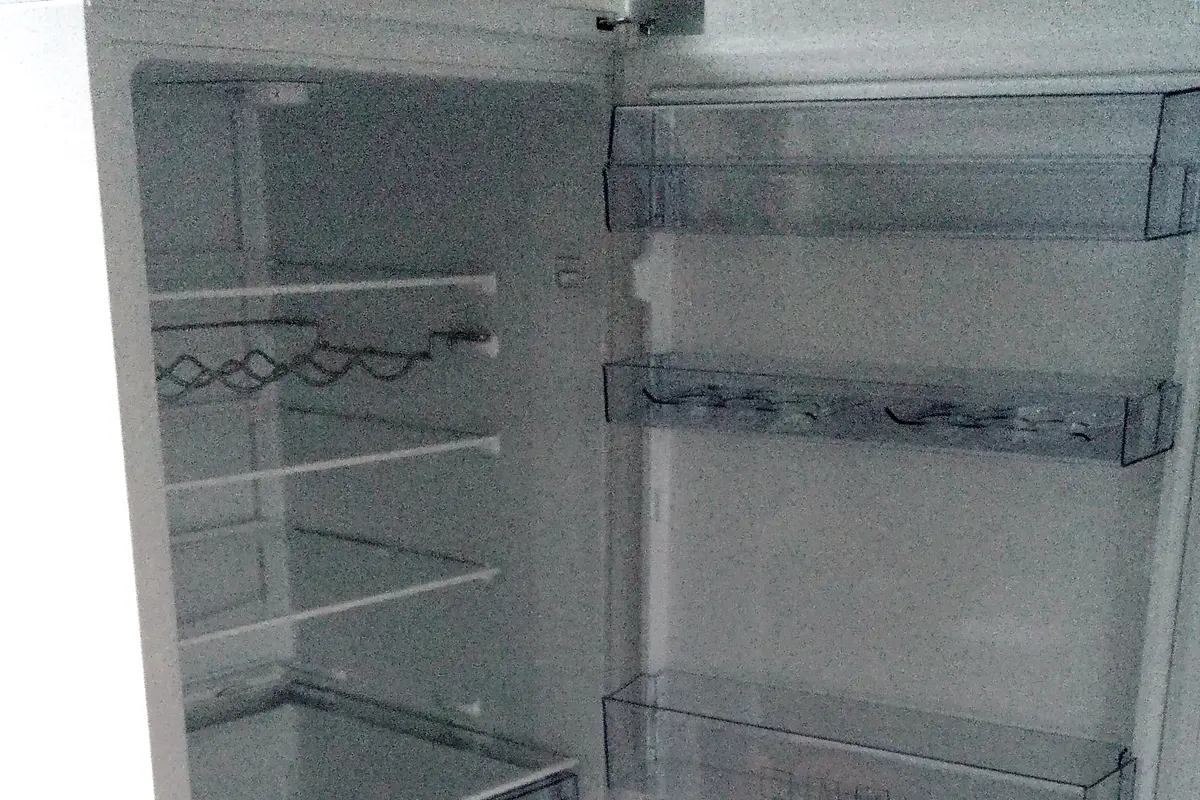 The inside of an empty fridge with its door open, showing clear glass shelves and empty door racks