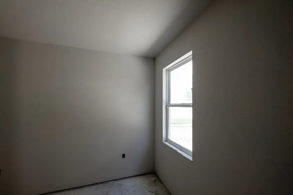 An empty room with bare walls and an uncovered floor, lit by a single window, with nothing left in it.