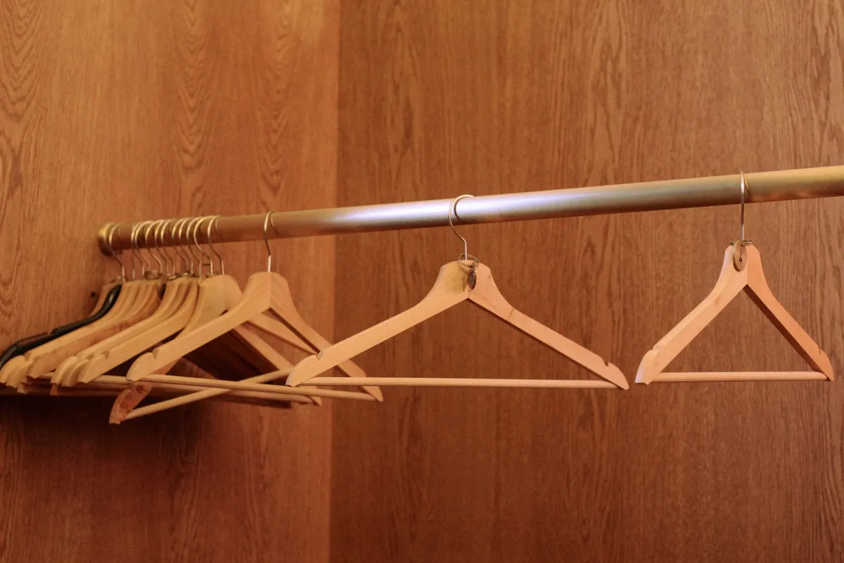 A row of empty wooden coat hangers left on the rail of a wood-panelled built-in wardrobe.