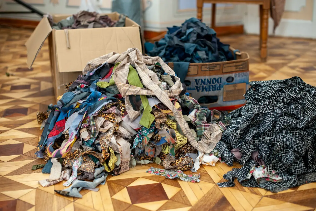 Piles of fabric offcuts separated by colour beside two cardboard boxes on a wooden parquet floor.