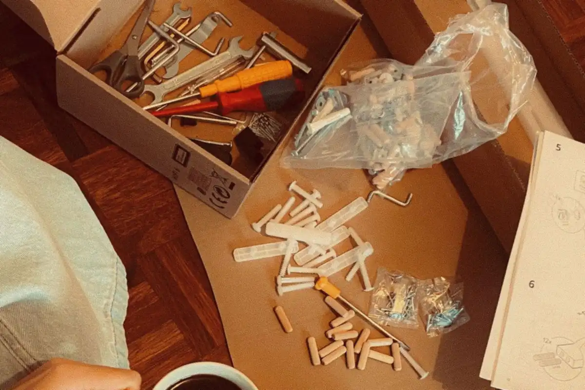 Wooden dowels, white cam bolts, a bag of fittings, a hex key and a box of screwdrivers and spanners spread across a flattened cardboard sheet.