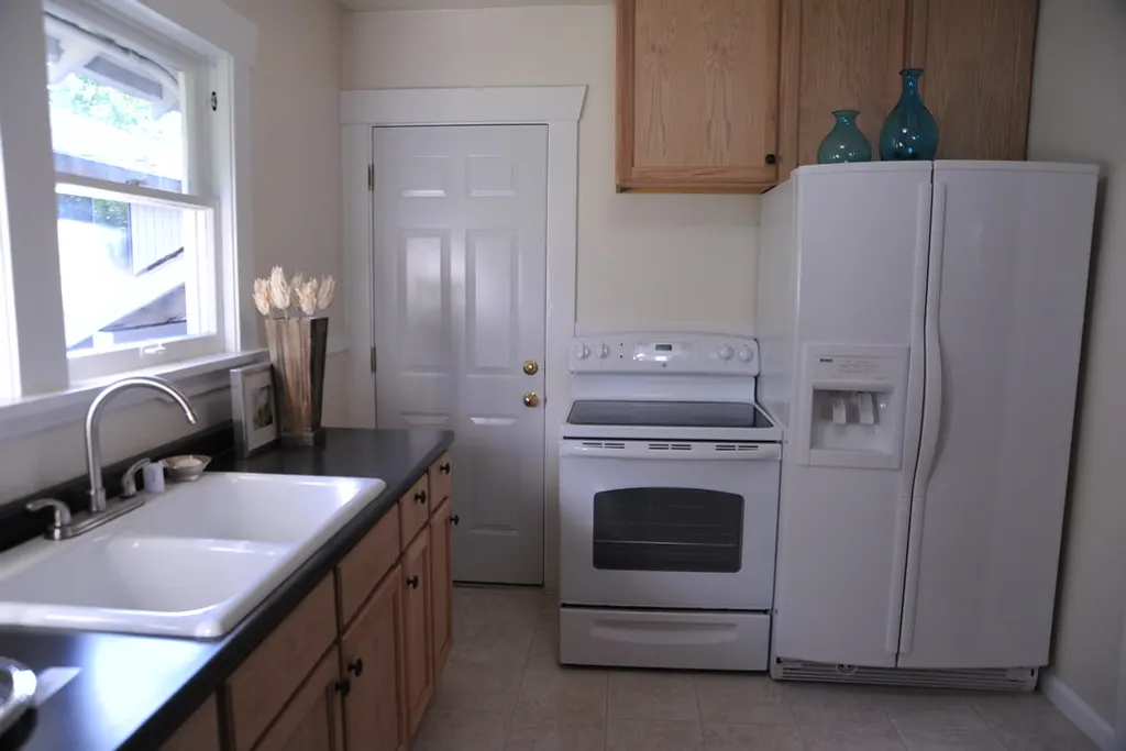A white side-by-side fridge freezer standing at the end of a run of kitchen units, next to the doorway it would have to be taken through.
