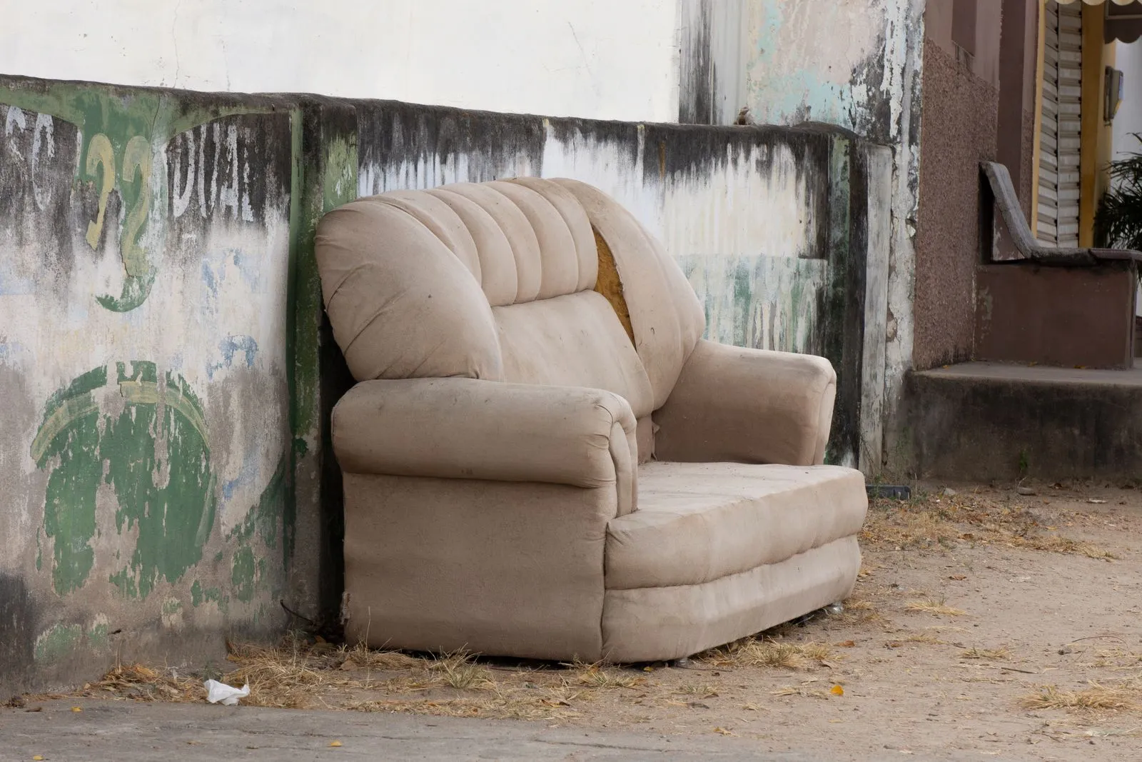 An old sofa left outdoors against a wall, ready for furniture disposal.