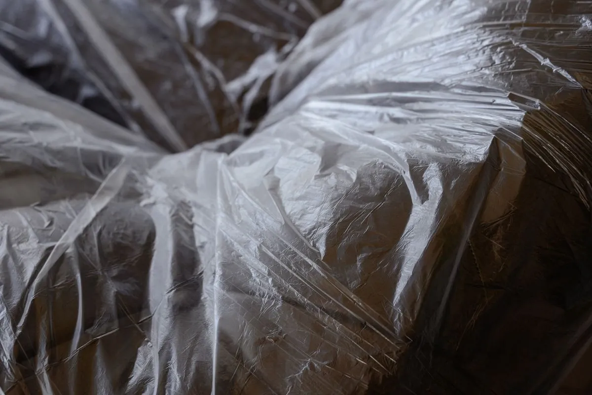 Clear plastic sheeting pulled tight and gathered over a large piece of upholstered furniture, wrapped closed before the item is moved.