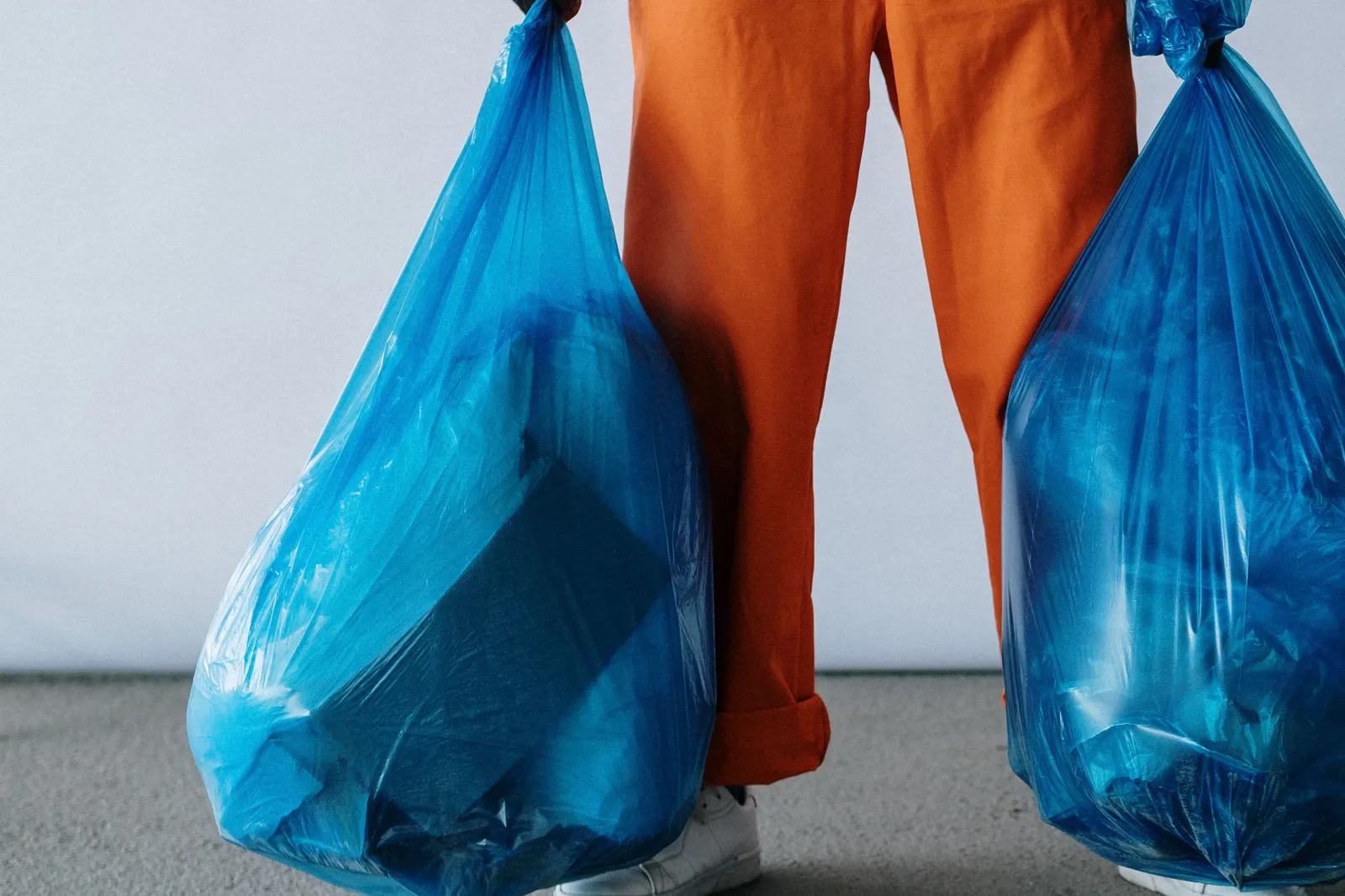 A person in overalls carrying two full garbage bags for collection.