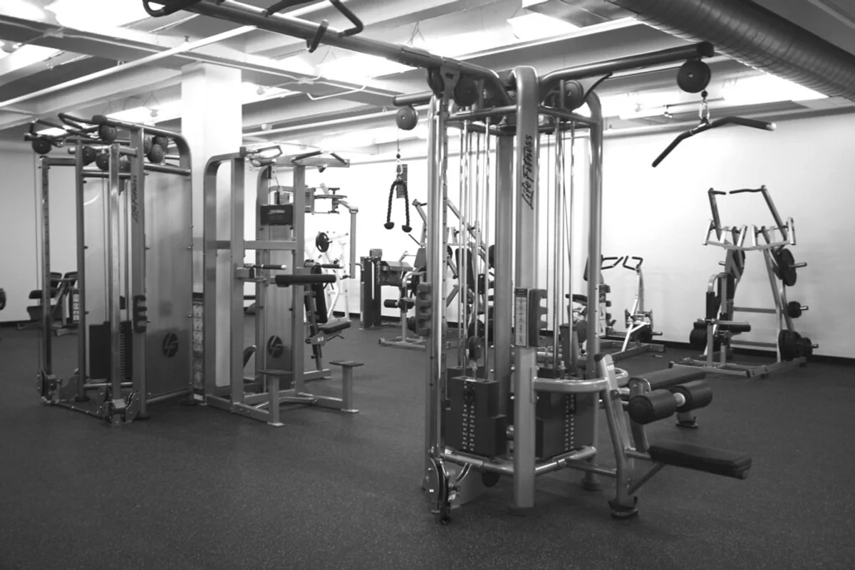 A commercial fitness gym facility equipped with resistance weight machines, weight benches, and cable equipment