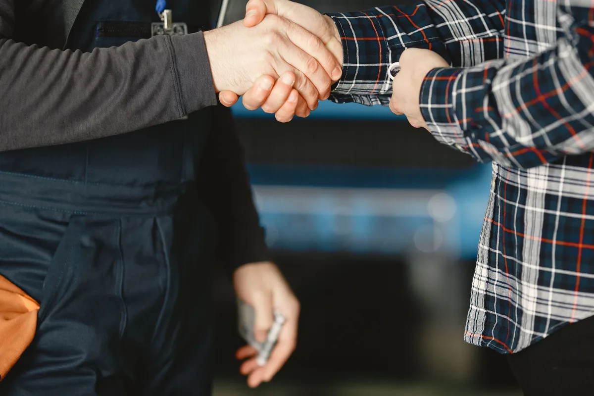 Close-up of a worker in overalls shaking hands with a customer.