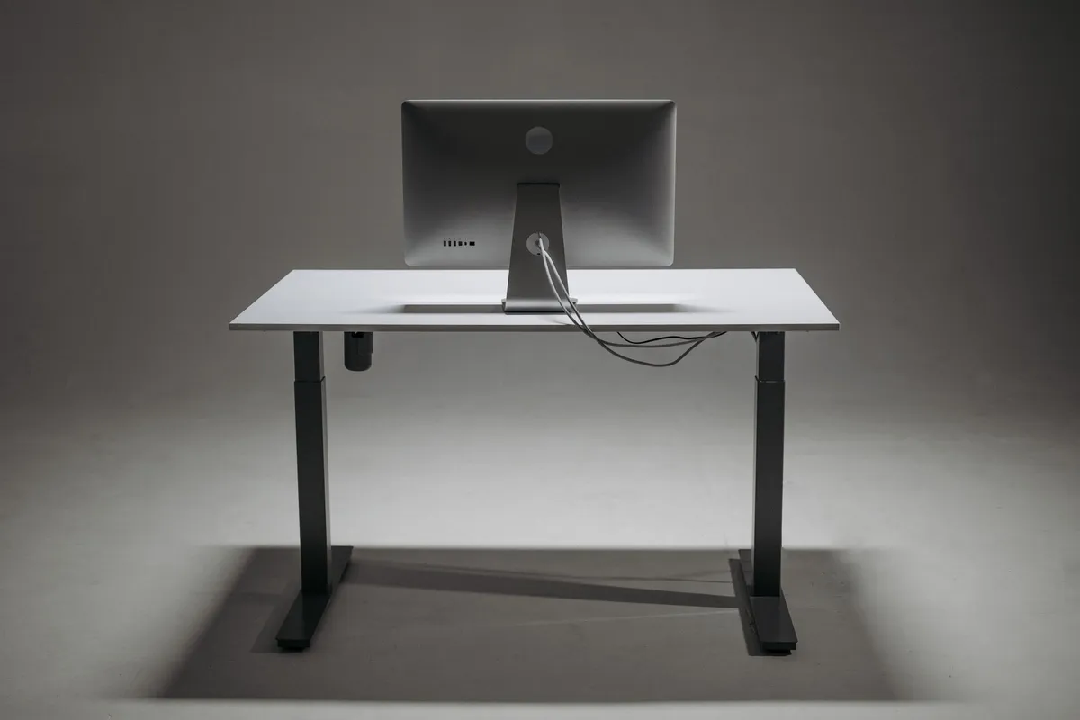 A height-adjustable standing desk photographed from behind, showing the two motorised columns, the control box under the top and the cables running between them.