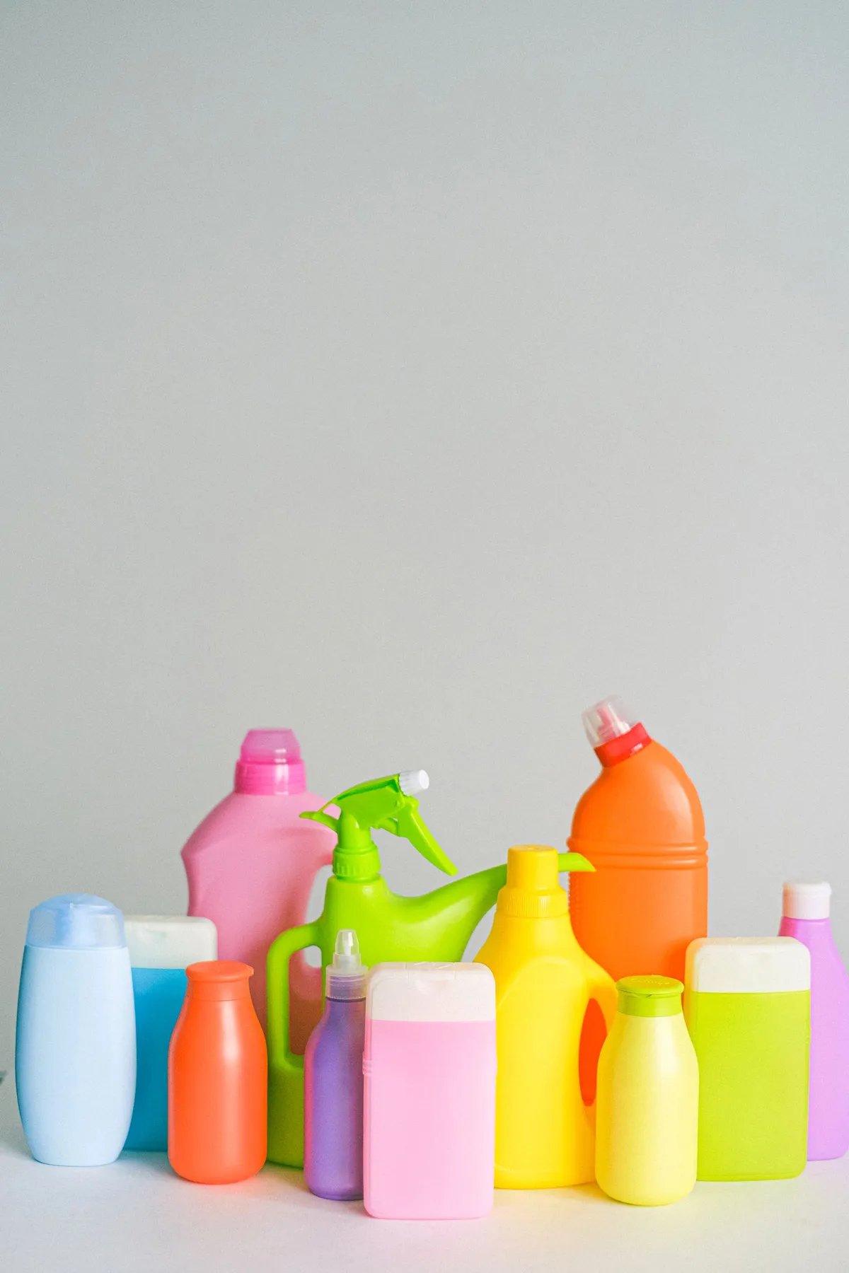 Rows of colourful household chemical and cleaning product bottles gathered together on a plain surface.