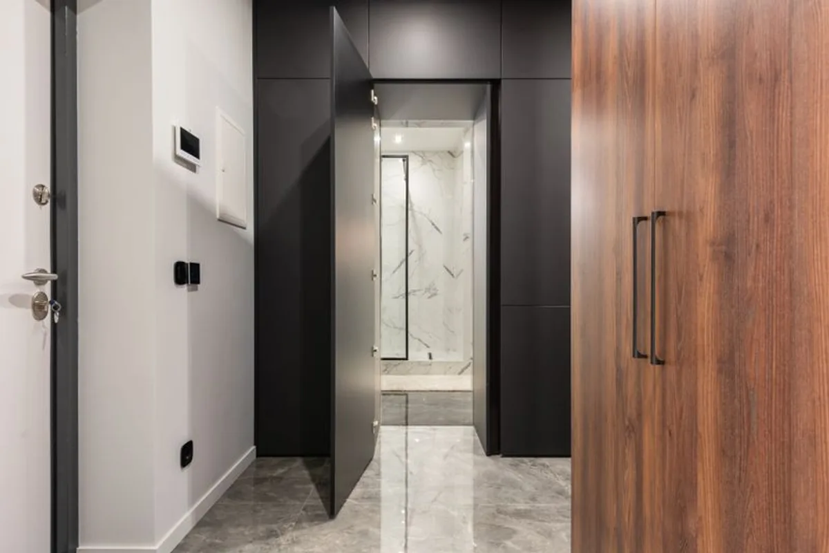 A polished marble-floored entrance hallway in an apartment, with a dark door open onto a marble-walled room and a walnut wardrobe to one side.