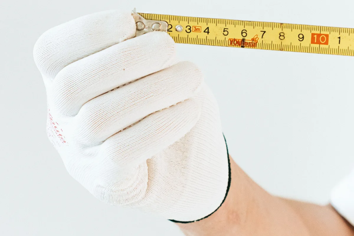 A gloved hand holding a metric tape measure extended for measuring furniture.