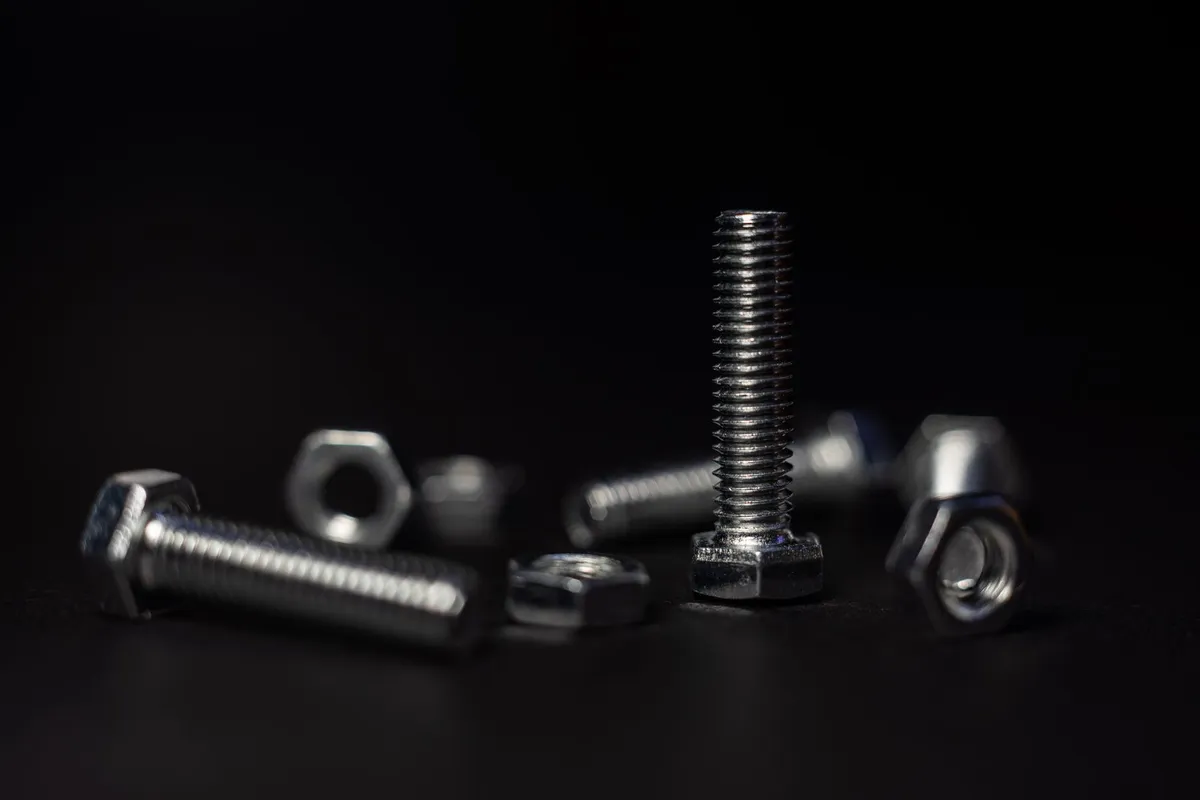 A close-up of loose metal nuts, bolts and screws scattered on a dark surface, the kind of small hardware separated out from a dismantled piece of furniture.