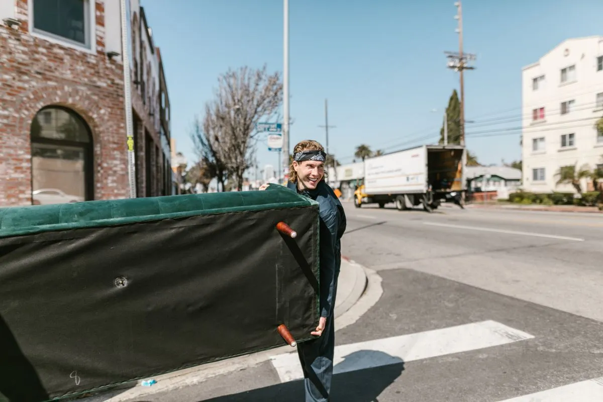 A worker carrying a large couch out of a building.