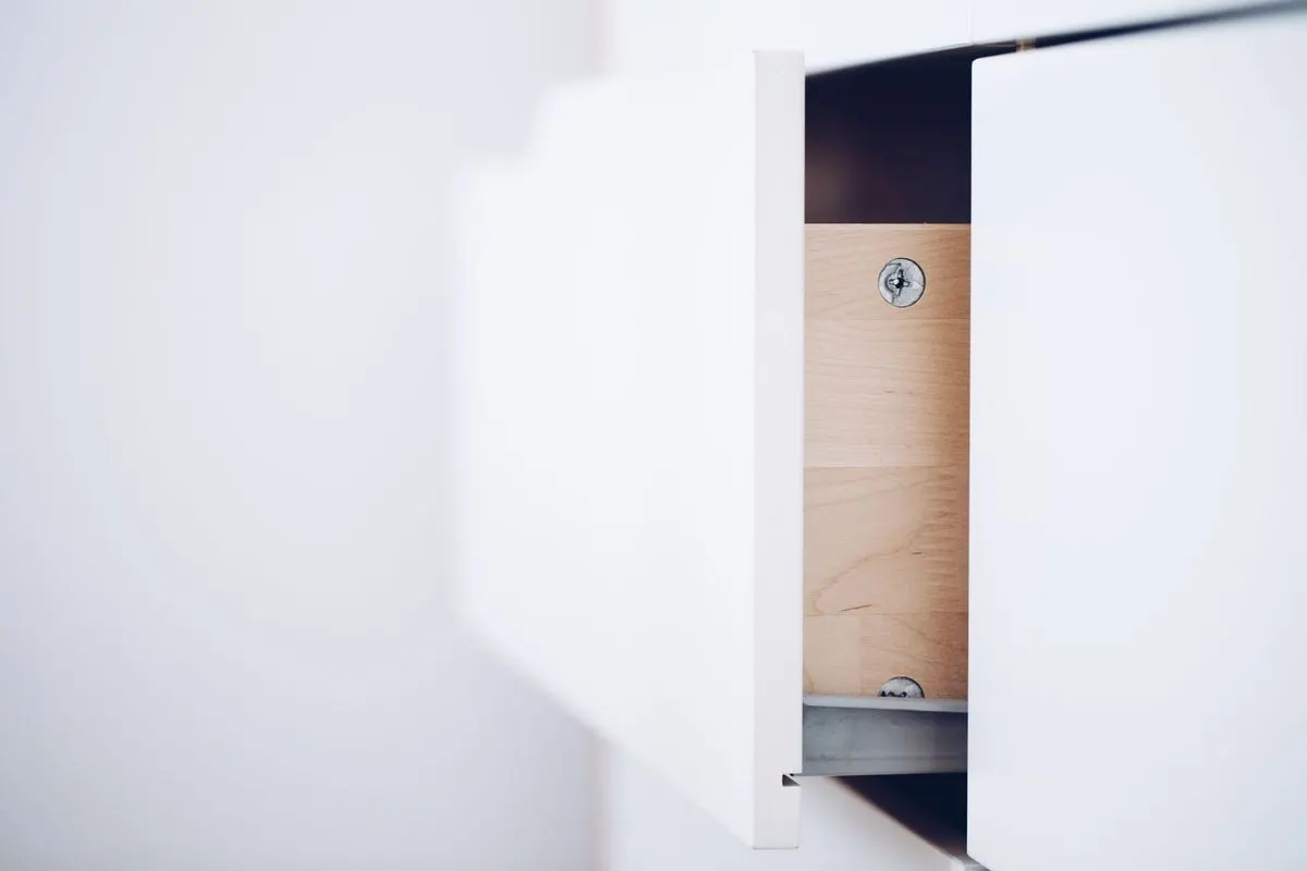 A white drawer pulled partly open, showing the bare timber side panel, a metal runner along the base and a single screw head near the top.