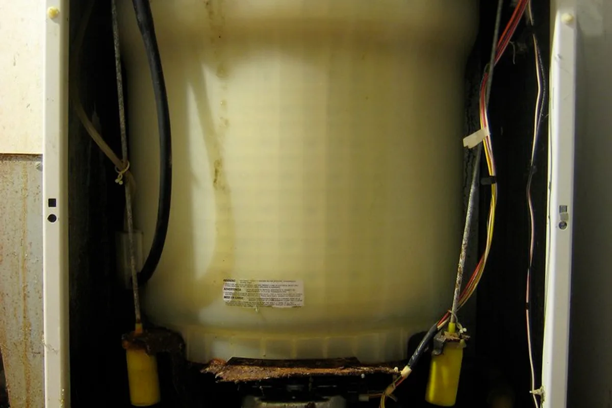 The internal drum, electric motor, and coiled wiring of a washing machine exposed after its outer casing has been removed.
