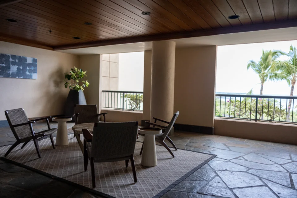 A set of outdoor lounge chairs and side tables on a covered villa terrace with palm trees beyond, the kind of items that have no place in an apartment.