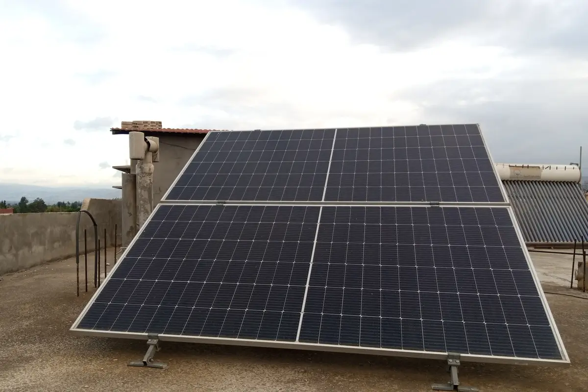 A four-panel solar array bolted to a galvanised steel frame on a flat concrete rooftop, with a solar water heater and its evacuated tubes behind it.