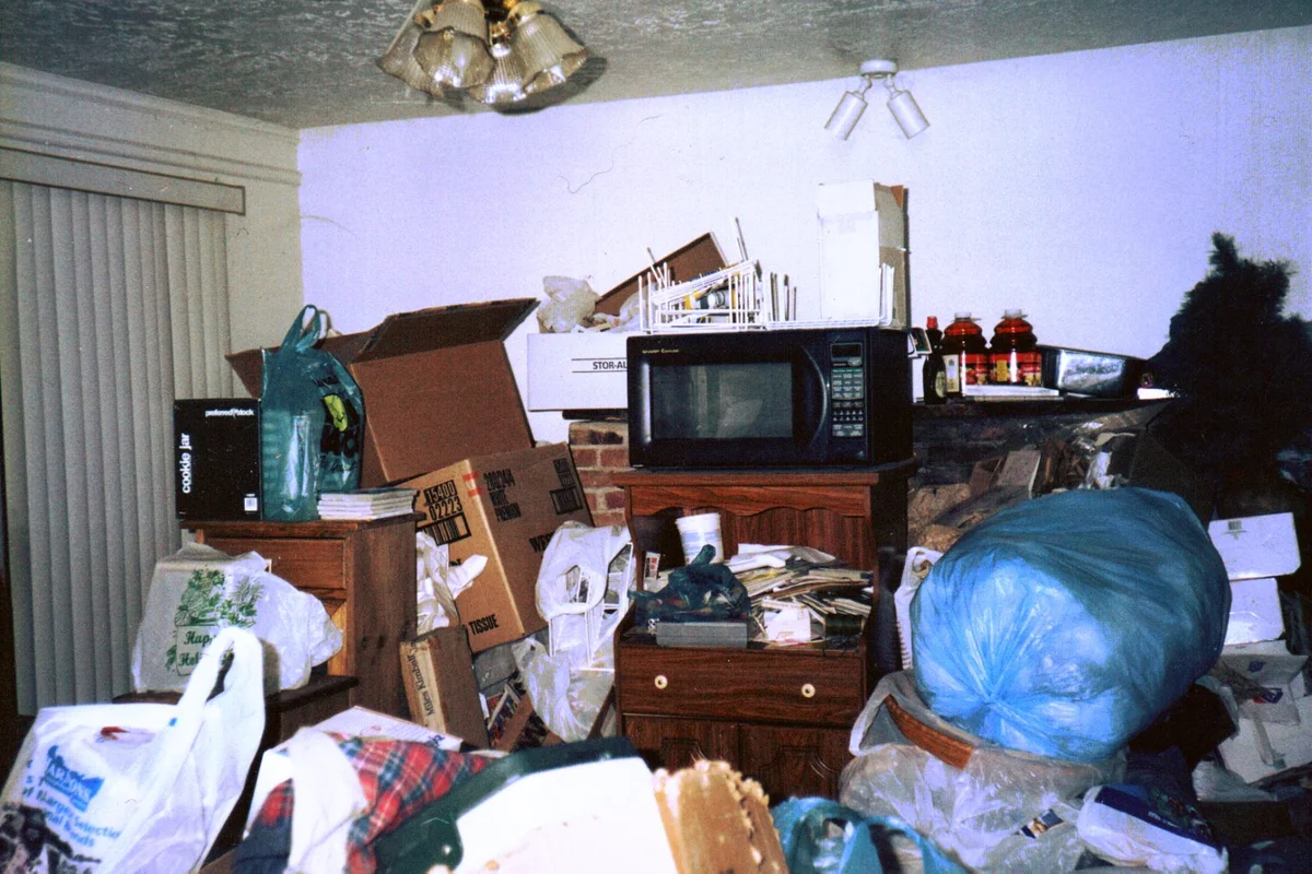 A living room piled high with boxes, bags and household belongings, leaving only a narrow path through it.