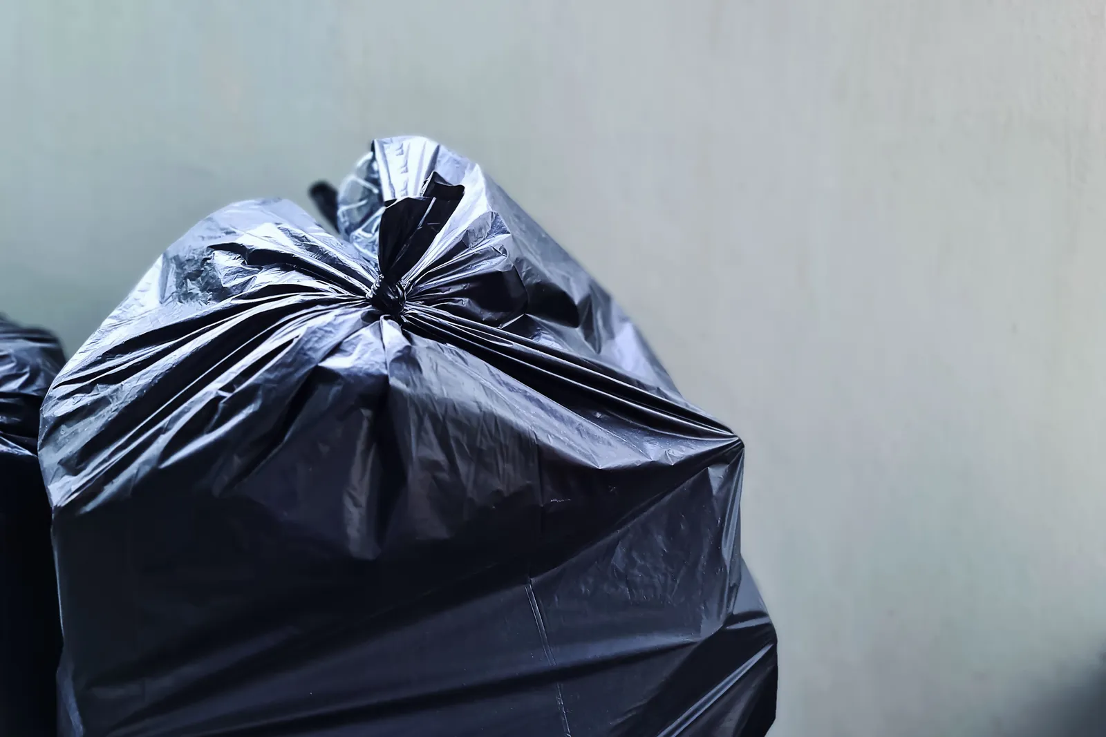 A large black rubbish bag ready for collection against a plain wall.
